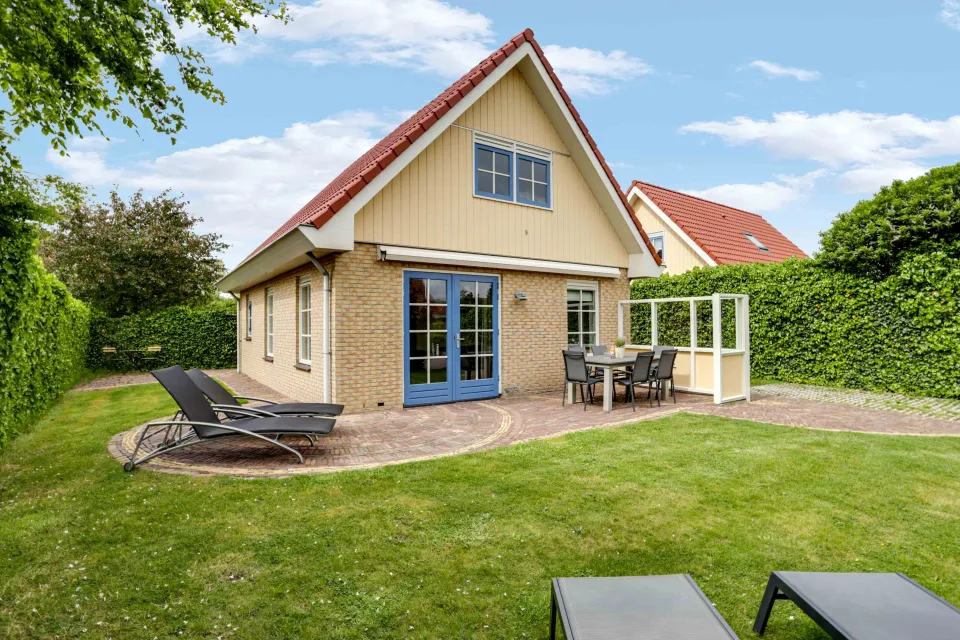 Vakantiewoning met serre, blauwe deuren en een terras met ligbedden in de tuin