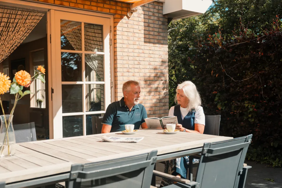 Ouder stel drinkt koffie aan de tuintafel naast de vakantiewoning