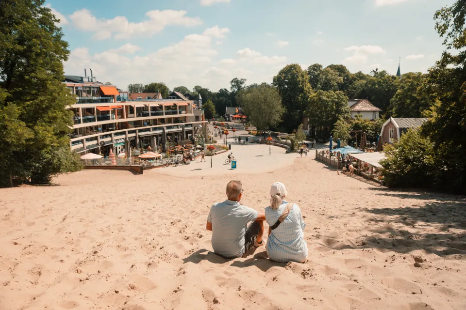 Ouder stel zit in het zand en kijkt uit over de terrassen van Schoorl