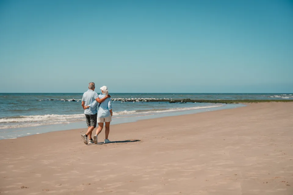 Ouder stel loopt samen langs de zee over het natte zand