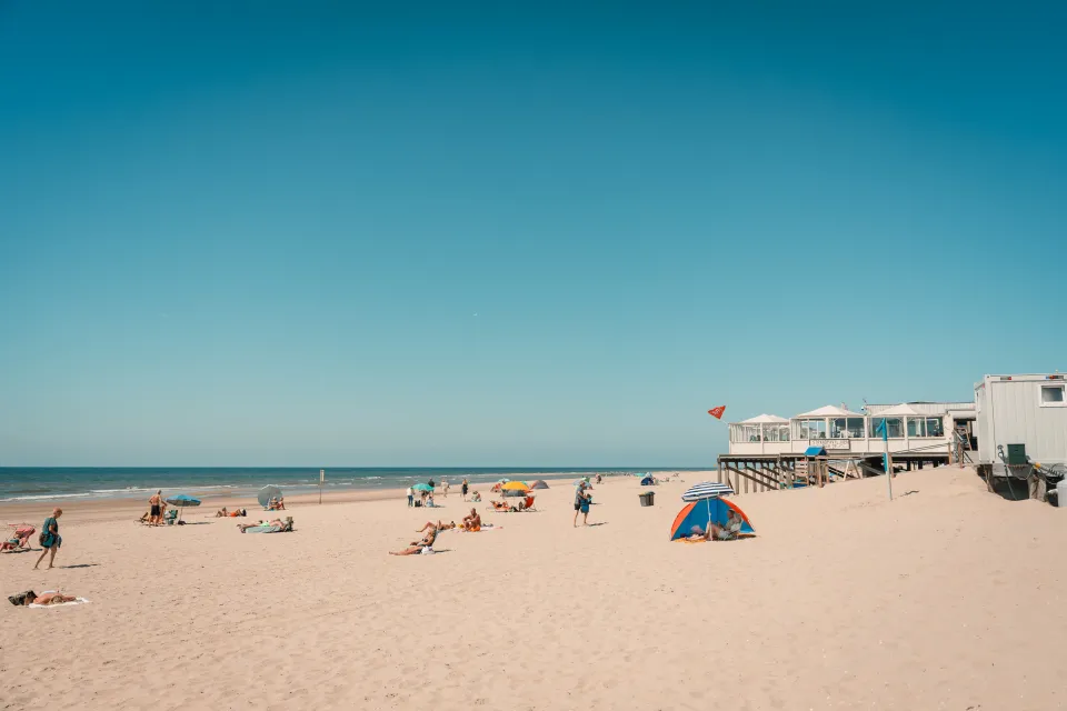 Strand met badgasten, windschermen en een strandpaviljoen aan de duinvoet