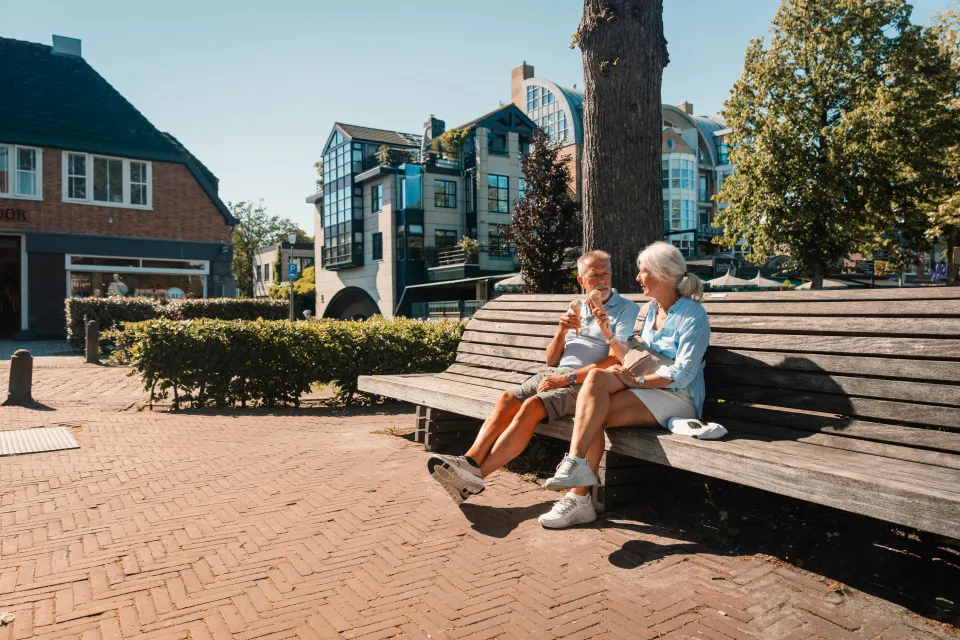 Ouder stel zit samen op een lange houten bank op het dorpsplein