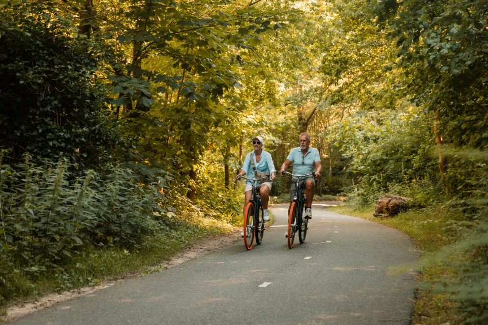 Ouder stel fietst over een slingerend bospad tussen het groen