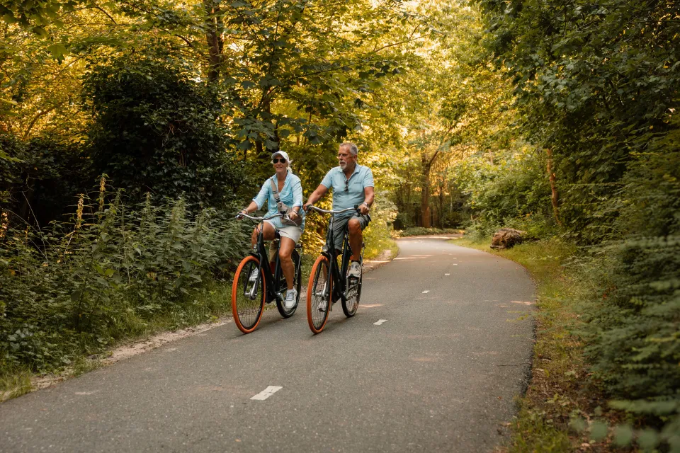 Ouder stel fietst samen over een slingerend pad door het duinbos