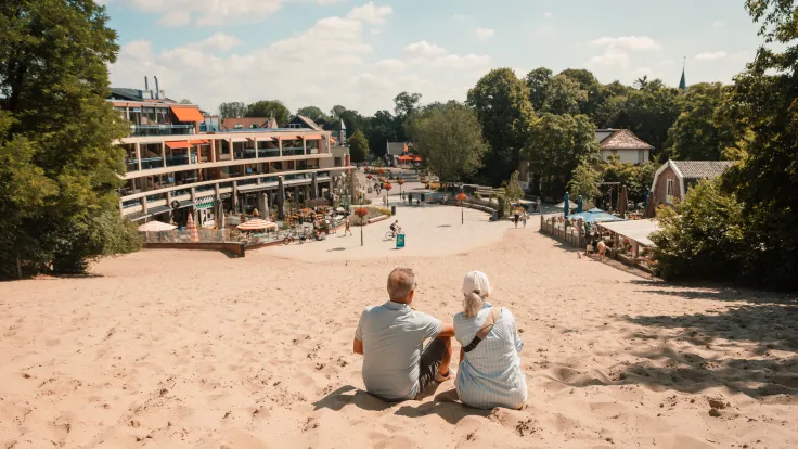 Ouder stel zit in het zand en kijkt uit over de terrassen van Schoorl