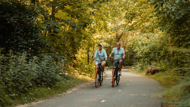 Ouder stel fietst over een slingerend bospad tussen het groen