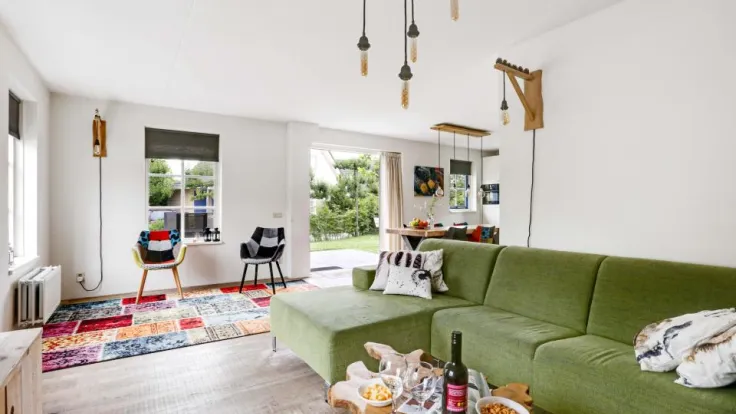 Woonkamer met groene bank, hanglampen en doorkijk naar de eethoek in een vakantiewoning